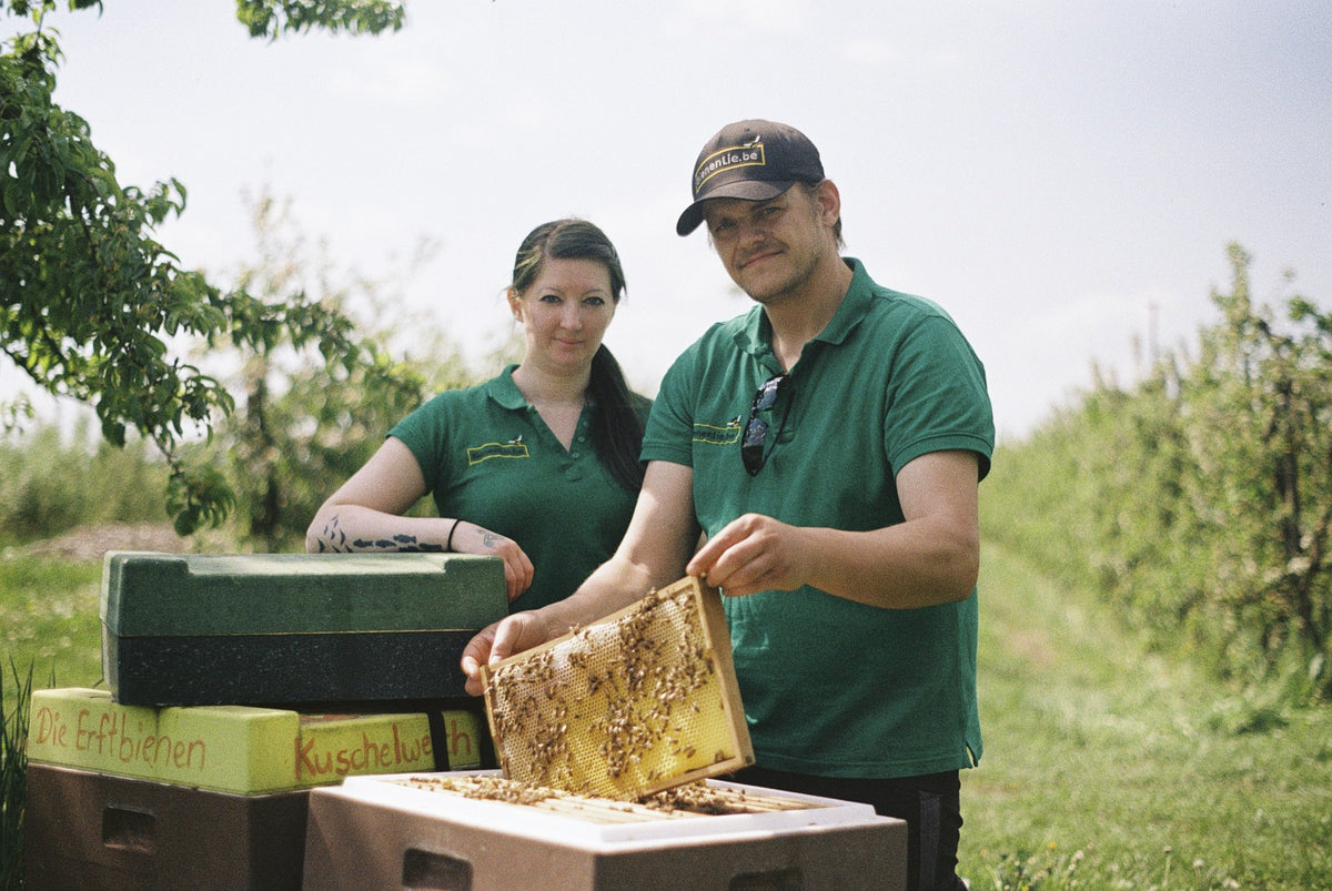 Zwei Menschen aus der Imkerei BienenLie.be mit einer Honigwabe am Bienenstock